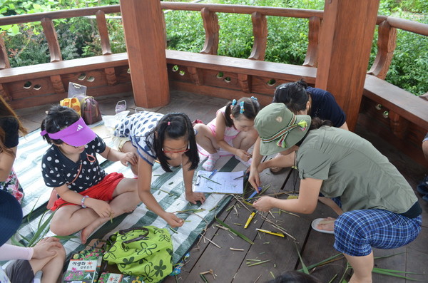 1학년 <생태학습 동아리> 어린이들과 엄마들이 갈대를 이용하여 풀피리 만들기에 열중하고 있다.(출처 :  김광철)