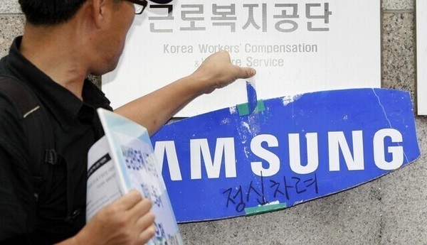 어떤 노동자가 서울 근로복지공단 표지판 위에 쪼개진 삼성전자 로고를 투명 테이프로 붙이고 있다. 박종식 기자 anaki@hani.co.kr, 한겨레, 2023.07.25.